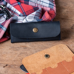 May include: Two leather wallets, one black and one brown, with multiple slots for cards and cash. The black wallet has a snap closure and a metal button.