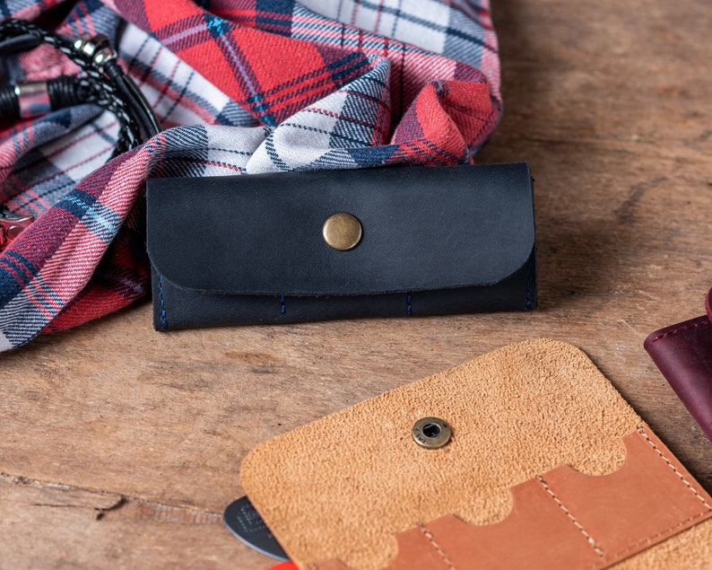 May include: Two leather wallets, one black and one brown, with multiple slots for cards and cash. The black wallet has a snap closure and a metal button.