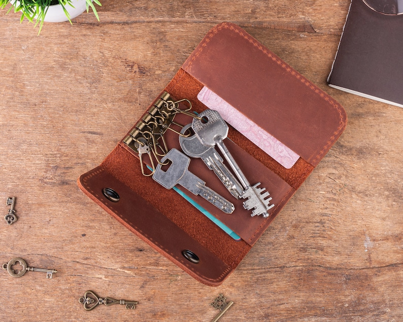 May include: A brown leather key holder with a key ring and multiple keys. The key holder has a flap that folds over the keys and a card slot.