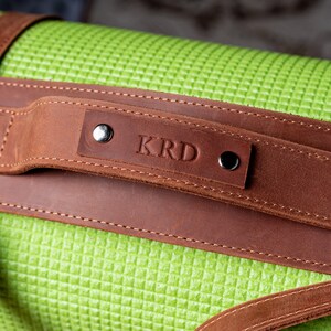 May include: A brown leather yoga mat strap with a personalised name, "KRD", embossed on the strap.