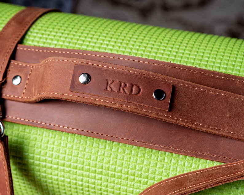 May include: A brown leather yoga mat strap with a personalised name, "KRD", embossed on the strap.