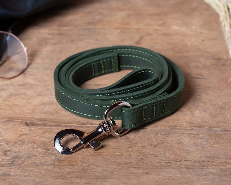 May include: A dark green leather dog leash with a silver metal clip. The leash is stitched with a light green thread.