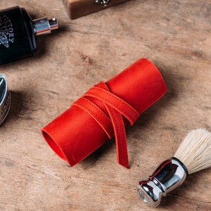 May include: A red leather roll with a white stitching detail, a silver shaving brush with white bristles, and a black bottle with the text "Victory Limited Edition" on the label.