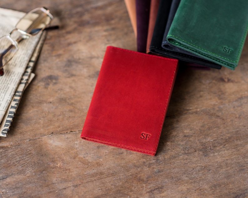 May include: A red leather wallet with the initials "SF" embossed on the front. The wallet is lying on a wooden surface.