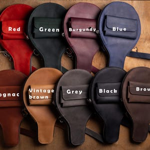 May include: A collection of leather bags in various colors, including red, green, burgundy, blue, cognac, vintage brown, grey, black, and brown. Each bag has a unique shape with a small front pocket and a zipper closure.