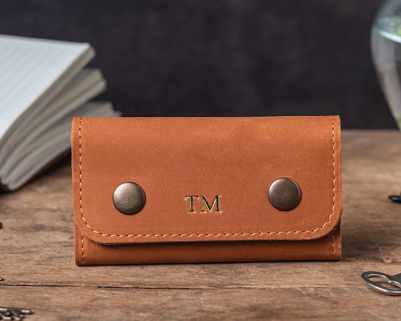 May include: A brown leather key holder with two metal snaps and the initials "TM" embossed in gold.