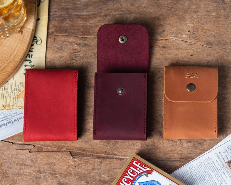 May include: Three leather card holders in different colors: red, burgundy, and brown. The brown card holder has the initials "AM" embossed on the front.
