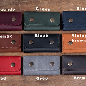 May include: Nine leather keychains in different colors, including burgundy, green, blue, cognac, black, vintage brown, red, grey, and brown. Each keychain has two metal snaps.