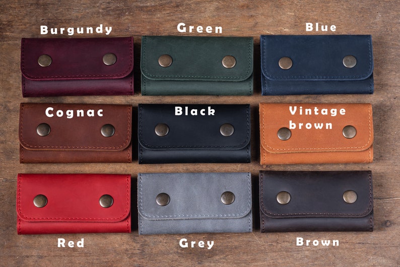 May include: Nine leather keychains in different colors, including burgundy, green, blue, cognac, black, vintage brown, red, grey, and brown. Each keychain has two metal snaps.