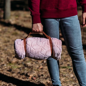 May include: A person carrying a rolled up pink blanket with a brown leather strap.