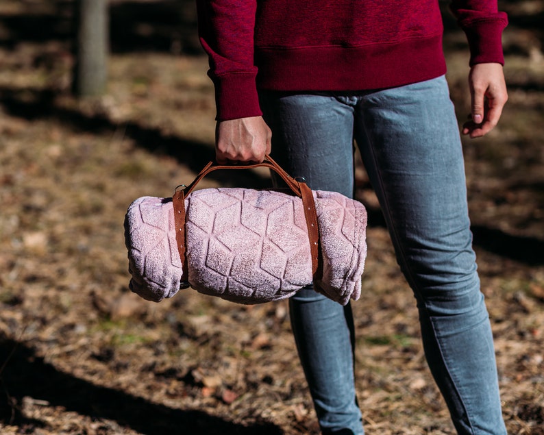 May include: A person carrying a rolled up pink blanket with a brown leather strap.