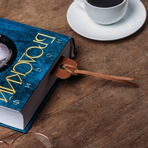 May include: A blue hardcover book with the title "Broca's Brain" in yellow lettering. A brown leather bookmark is attached to the book.