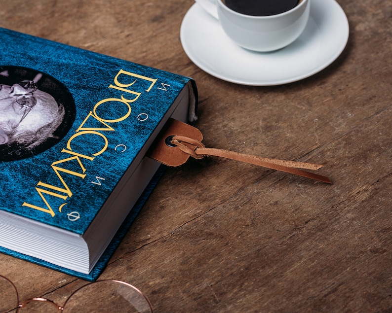May include: A blue hardcover book with the title "Broca's Brain" in yellow lettering. A brown leather bookmark is attached to the book.