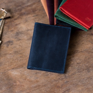 May include: A dark blue leather wallet with blue stitching. The wallet is lying on a wooden surface.