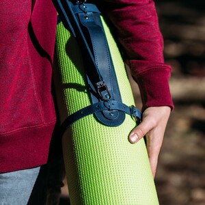 May include: A person carrying a green yoga mat with a dark blue leather strap and buckle.