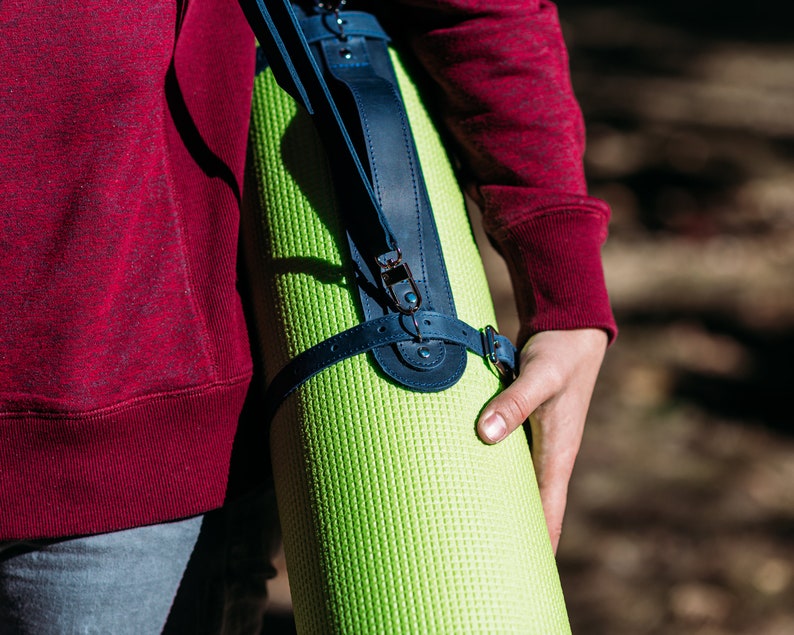 May include: A person carrying a green yoga mat with a dark blue leather strap and buckle.