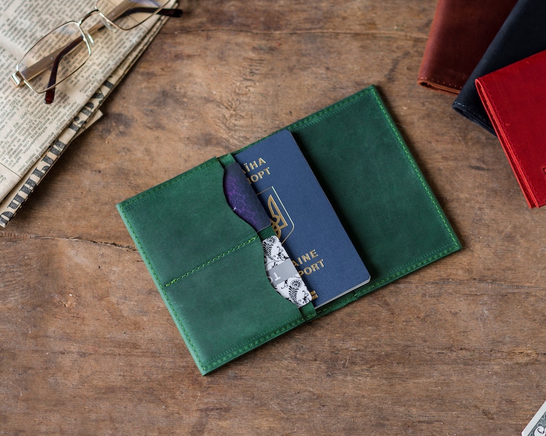May include: A green leather passport holder with a blue passport inside. The passport has the text "UKRAINE PASSPORT" on the cover.