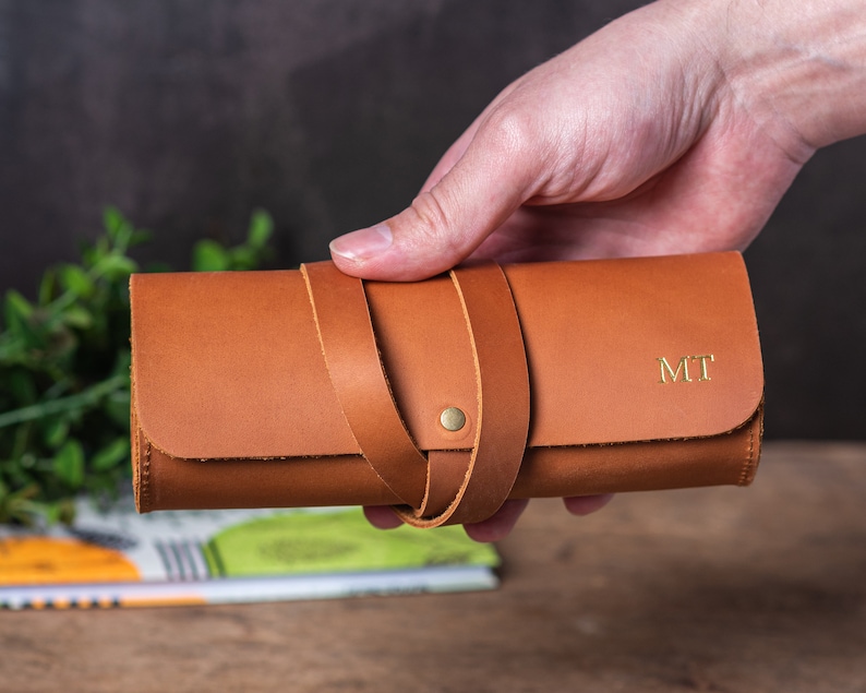 May include: A brown leather pencil case with a strap closure and the initials "MT" embossed in gold.