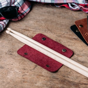 May include: A burgundy leather case with two wooden drumsticks inside. The case has a flap that closes with a snap.