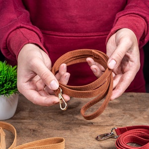 May include: A brown leather strap with a gold metal clasp. The strap is folded in a circle and held in someone's hands.