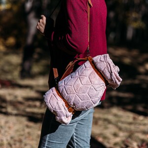 May include: A person wearing a red shirt carries a pink and brown patterned blanket strapped to their shoulder with a brown leather strap.