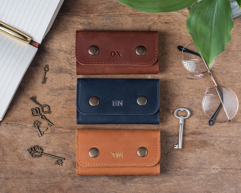 May include: Three leather keychains with initials 'OX', 'BN', and 'TM' embossed on them. The keychains are brown, navy blue, and tan.