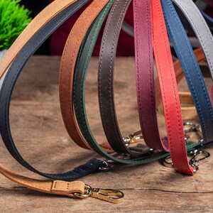 May include: A collection of eight leather straps in various colours, including brown, red, green, blue, and black. The straps are arranged in a semi-circle, with the ends of each strap overlapping. The straps are all stitched with a decorative stitch.