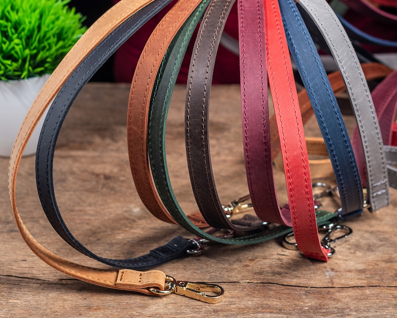 May include: A collection of eight leather straps in various colours, including brown, red, green, blue, and black. The straps are arranged in a semi-circle, with the ends of each strap overlapping. The straps are all stitched with a decorative stitch.