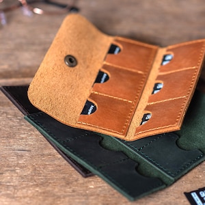 May include: A brown leather case with six slots for memory cards, folded over a green leather case with six slots for memory cards.