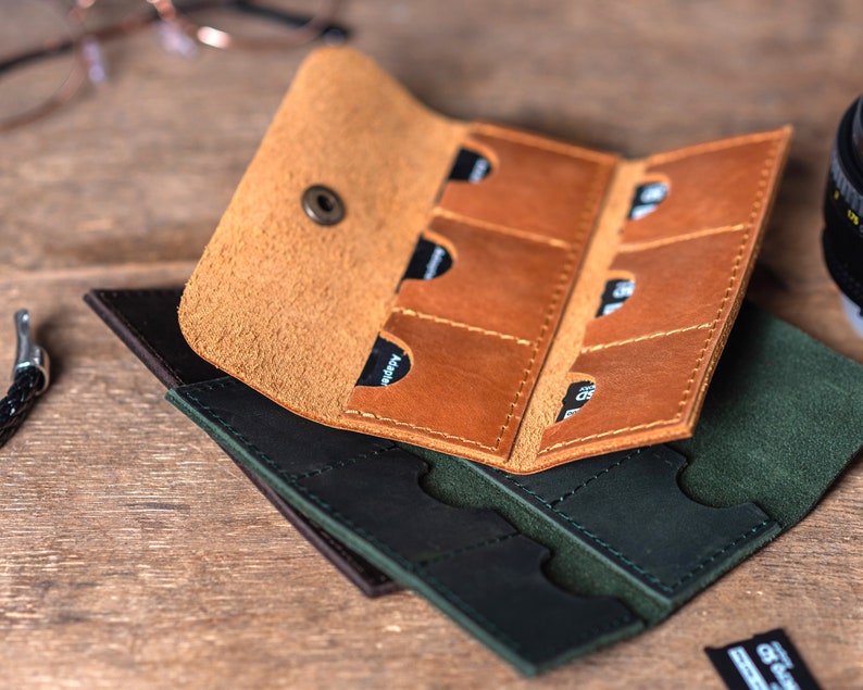 May include: A brown leather case with six slots for memory cards, folded over a green leather case with six slots for memory cards.