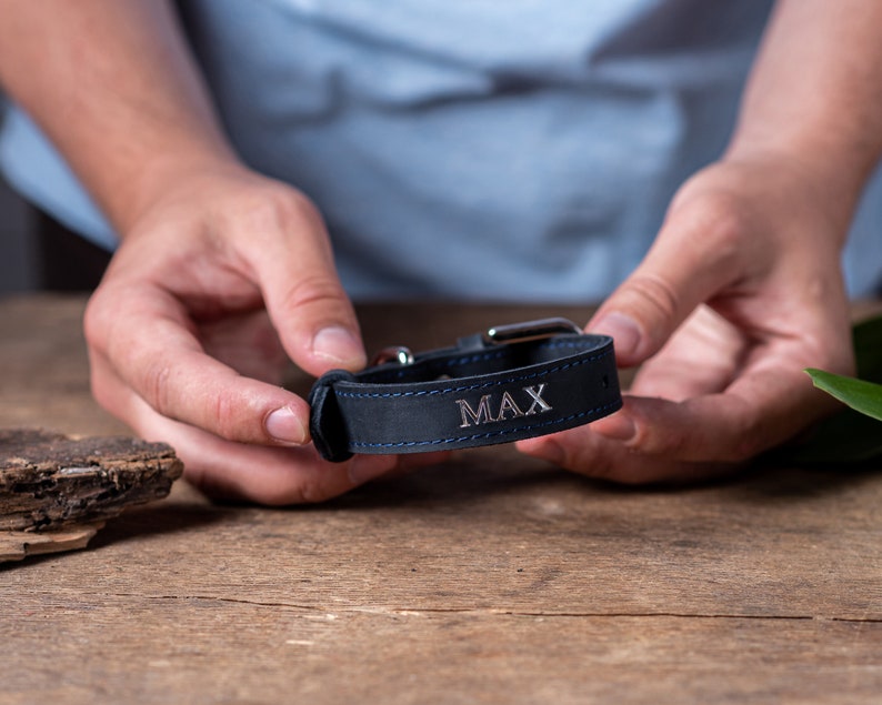 May include: A dark blue leather dog collar with silver hardware and the name "MAX" engraved on it.