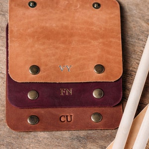 May include: Three leather keyrings with brass rivets and engraved initials. The top keyring is brown with the initials "VY", the middle keyring is burgundy with the initials "FN", and the bottom keyring is brown with the initials "CU".