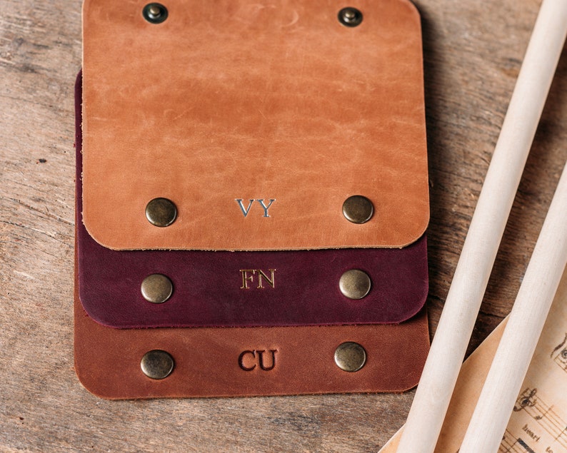 May include: Three leather keyrings with brass rivets and engraved initials. The top keyring is brown with the initials "VY", the middle keyring is burgundy with the initials "FN", and the bottom keyring is brown with the initials "CU".