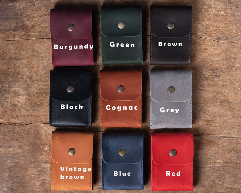 May include: Ten leather card holders in different colors, including burgundy, green, brown, black, cognac, grey, vintage brown, blue, and red. Each holder has a single snap closure.