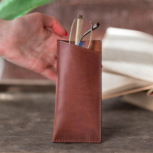 May include: A brown leather glasses case with a pair of glasses inside. The case has a flap that closes with a snap.
