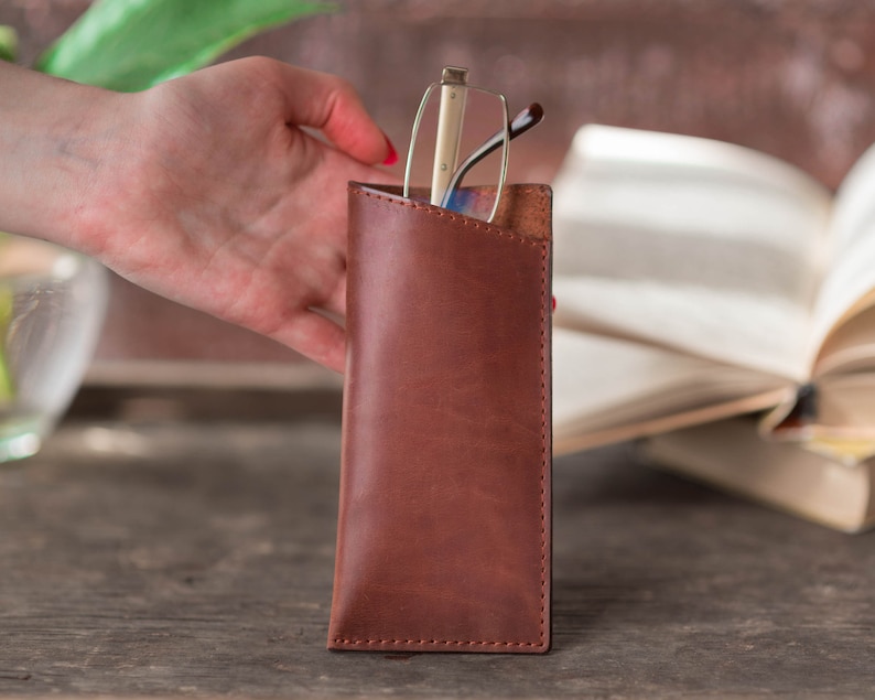 May include: A brown leather glasses case with a pair of glasses inside. The case has a flap that closes with a snap.