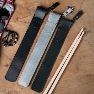 Puede incluir: Tres estuches de cuero para baquetas de bater&iacute;a en negro, gris y verde oscuro, con un par de baquetas de madera.