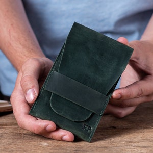 May include: A dark green leather wallet with a flap closure and a single strap. The wallet has the initials "FP" embossed on the front.
