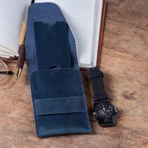 May include: A blue leather wallet with a flap closure and a watch with a black band and a silver face.