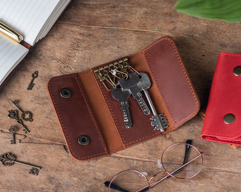 May include: A brown leather key holder with multiple keys attached to a key ring. The key holder has a flap that folds over to secure the keys.