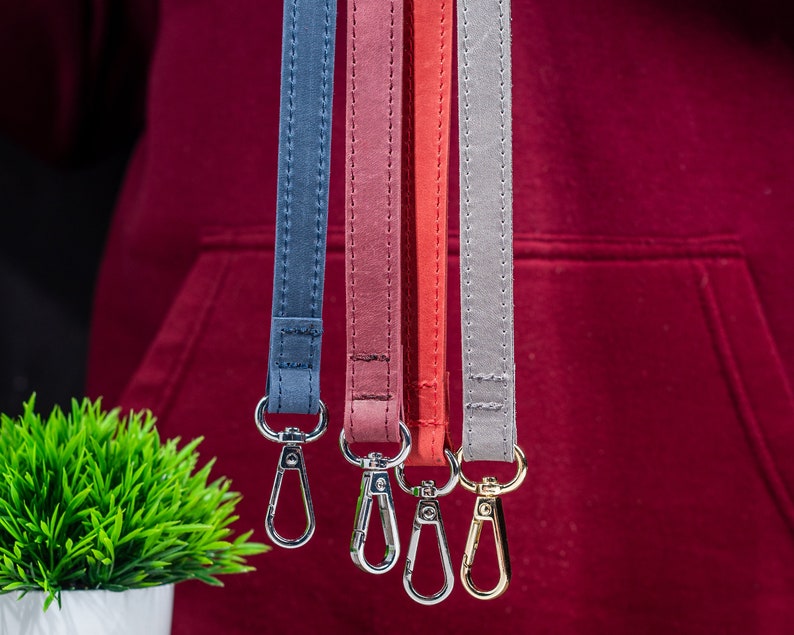 May include: Four different coloured lanyards with gold metal clasps. The lanyards are blue, red, pink, and grey.