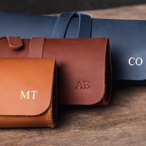 May include: Three leather pouches with personalised initials. The pouches are brown, tan, and dark blue. The initials are "MT", "AB", and "CO".
