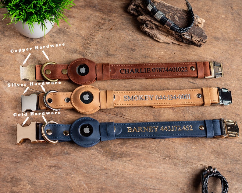May include: Three leather dog collars in brown, tan, and navy blue, each with a metal buckle and a circular holder for a tracking device. The brown collar has copper hardware and the name "CHARLIE" and a phone number. The tan collar has silver hardware and the name "SMOKEY" and a phone number. The navy blue collar has gold hardware and the name "BARNEY" and a phone number.