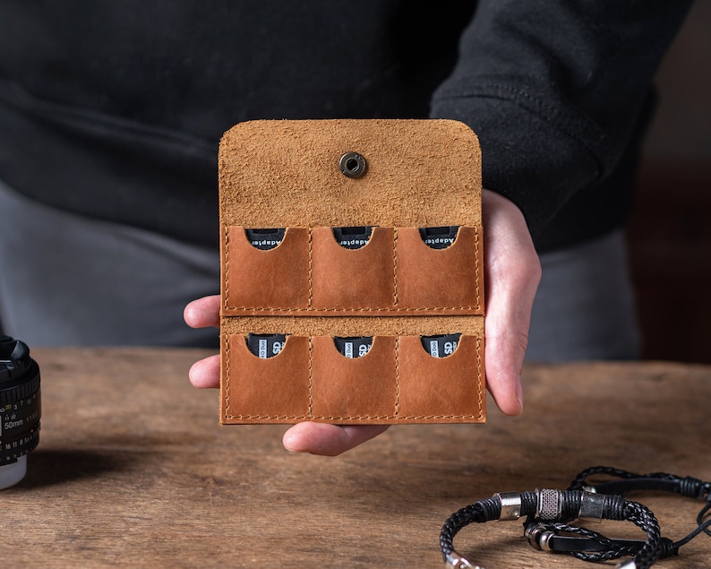 May include: A brown leather case with eight slots for memory cards. The case is open and the slots are empty.