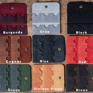 May include: Nine leather card holders in different colors, including burgundy, grey, black, cognac, blue, red, green, vintage brown, and brown. Each holder has six slots for cards.