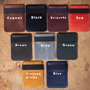 May include: A collection of leather cardholders in various colors, including cognac, black, burgundy, red, brown, grey, green, vintage brown, and blue. Each cardholder features a black elastic band and the color name in white text.