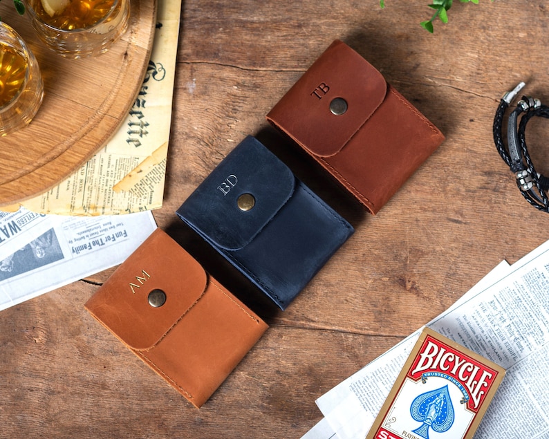 May include: Three leather card holders with a flap closure and a button. The card holders are brown, blue, and brown. Each card holder has a different monogram on the front: "TB", "BD", and "MV".