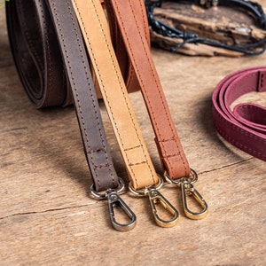 May include: Three leather straps with gold-toned clasps. The straps are brown, tan, and burgundy.