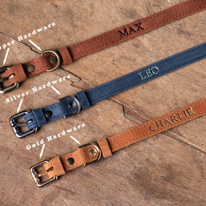 May include: Three leather dog collars with different hardware finishes. The top collar is brown with copper hardware and the name "MAX" engraved on it. The middle collar is blue with silver hardware and the name "LEO" engraved on it. The bottom collar is brown with gold hardware and the name "CHARLIE" engraved on it.
