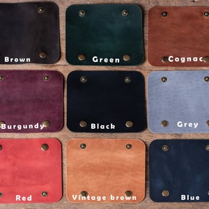 May include: Nine leather swatches in different colours, including brown, green, cognac, burgundy, black, grey, red, vintage brown, and blue. Each swatch has two brass rivets on the top and bottom.